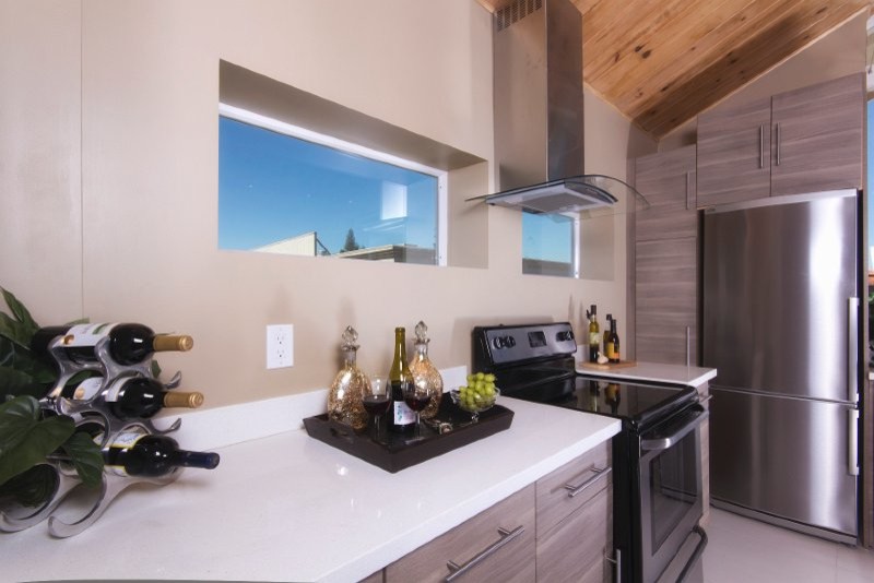 This is an example of a mid-sized contemporary l-shaped eat-in kitchen in San Francisco with a triple-bowl sink, flat-panel cabinets, medium wood cabinets, glass benchtops, beige splashback, stone slab splashback, stainless steel appliances and ceramic floors.