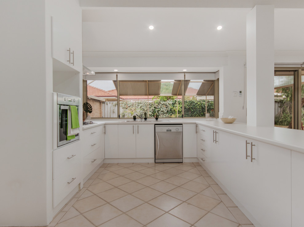 Photo of a large beach style u-shaped open plan kitchen in Perth with a double-bowl sink, flat-panel cabinets, white cabinets, laminate benchtops, white splashback, subway tile splashback, stainless steel appliances, ceramic floors, with island and beige floor.