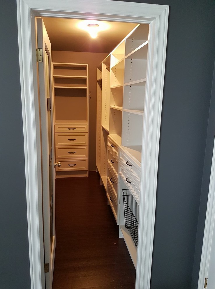 This is an example of a large traditional gender-neutral walk-in wardrobe in Other with flat-panel cabinets, white cabinets, laminate floors and brown floor.
