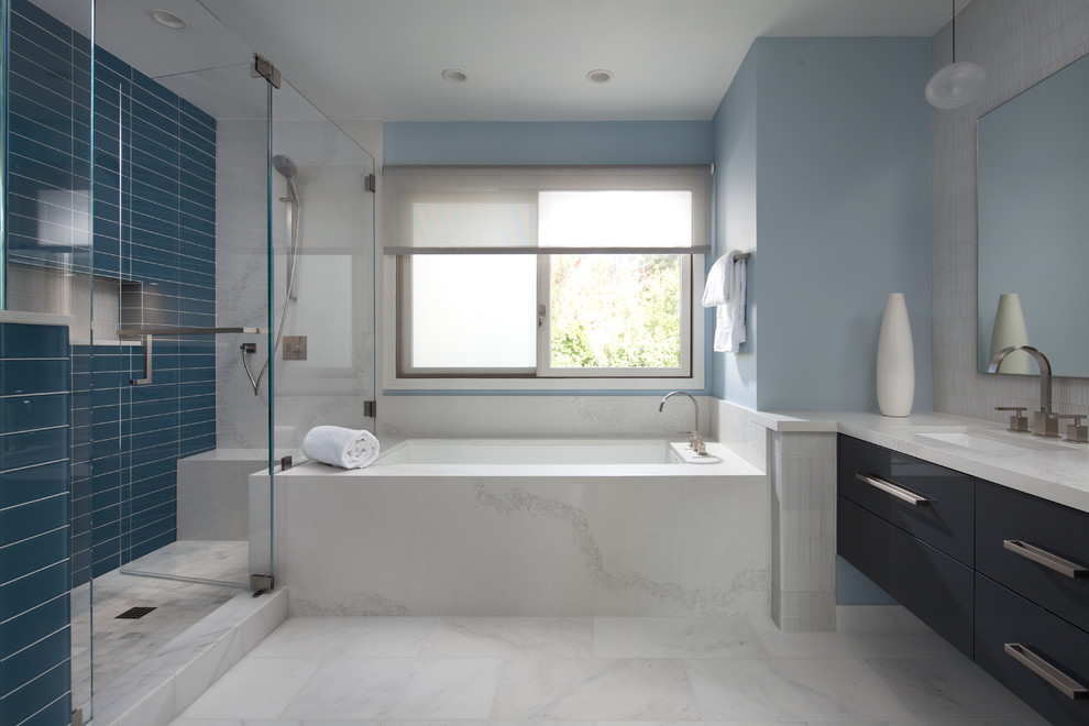 This is an example of a mid-sized modern master bathroom in San Francisco with beaded inset cabinets, grey cabinets, a drop-in tub, a corner shower, a one-piece toilet, beige tile, glass tile, blue walls, marble floors, an integrated sink, engineered quartz benchtops, white floor and a hinged shower door.