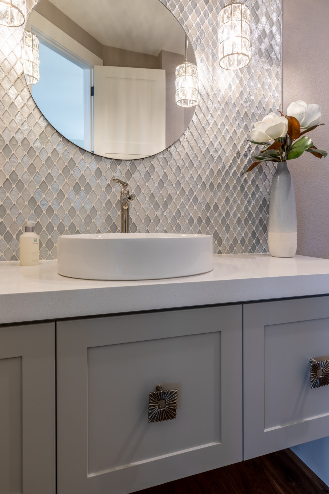 Inspiration for a large beach style powder room in Denver with shaker cabinets, grey cabinets, blue tile, glass sheet wall, grey walls, light hardwood floors, a vessel sink, engineered quartz benchtops, white benchtops and a floating vanity.