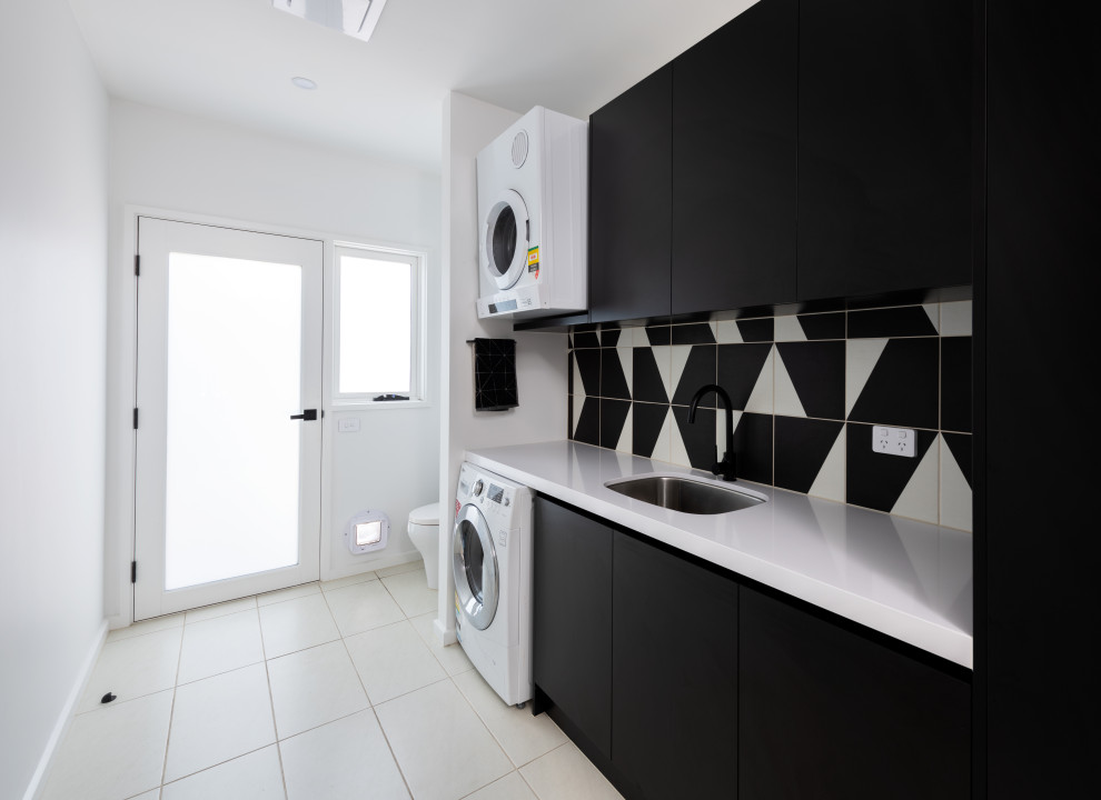 Mid-sized single-wall laundry room in Melbourne with an undermount sink, black cabinets, quartz benchtops, porcelain splashback, porcelain floors, a stacked washer and dryer, white floor and white benchtop.