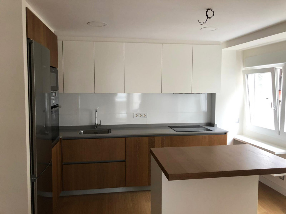 Mid-sized modern l-shaped separate kitchen in Bilbao with a single-bowl sink, flat-panel cabinets, medium wood cabinets, stainless steel appliances, medium hardwood floors, with island, brown floor and grey benchtop.