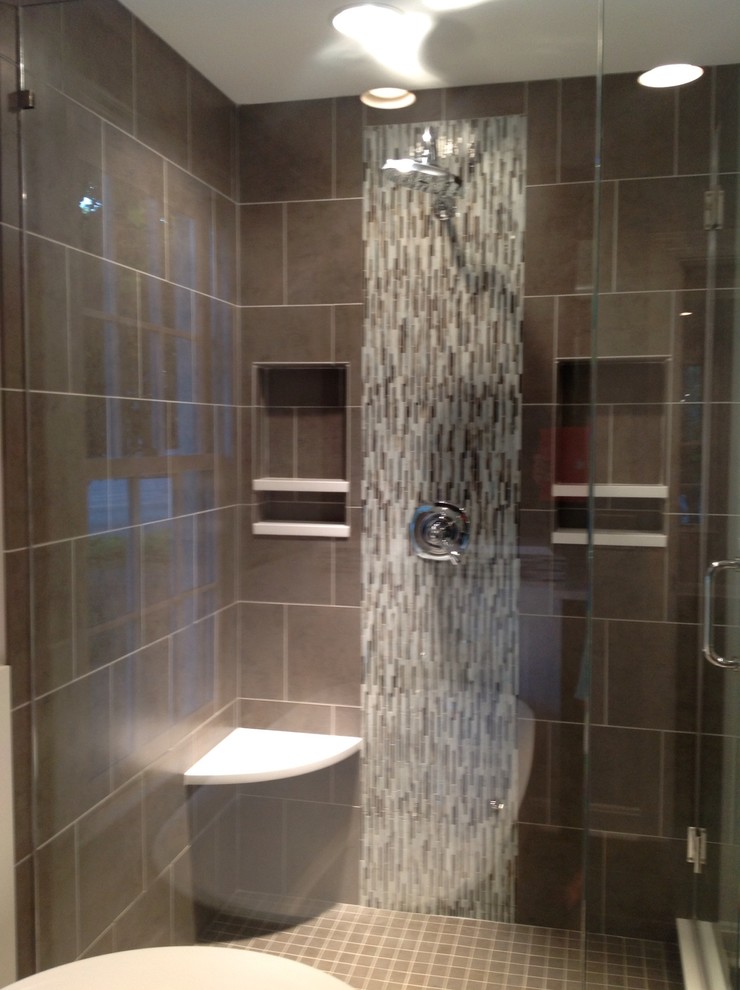 Photo of a contemporary bathroom in Nashville with an undermount sink, recessed-panel cabinets, brown cabinets, engineered quartz benchtops, a freestanding tub, a corner shower, a two-piece toilet, gray tile and glass tile.