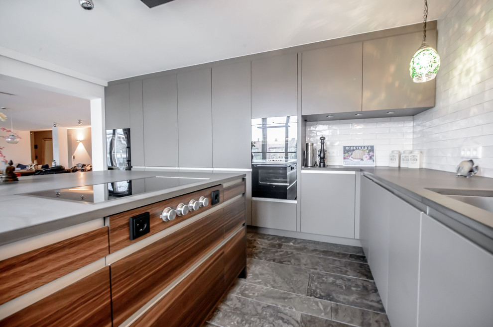 Large contemporary open plan kitchen in Munich with flat-panel cabinets, grey cabinets, white splashback, subway tile splashback, black appliances and with island.