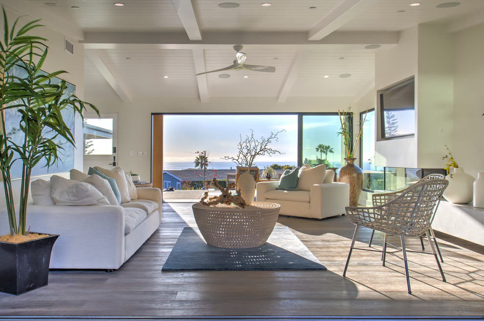 Design ideas for an expansive beach style open concept family room in Orange County with beige walls, dark hardwood floors, a standard fireplace, a plaster fireplace surround, a built-in media wall and brown floor.