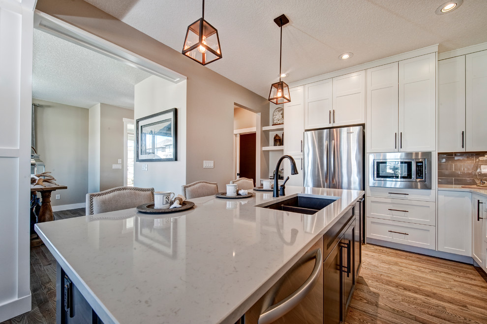 Photo of a contemporary eat-in kitchen in Calgary with a double-bowl sink, granite benchtops, grey splashback, ceramic splashback, stainless steel appliances, light hardwood floors and with island.