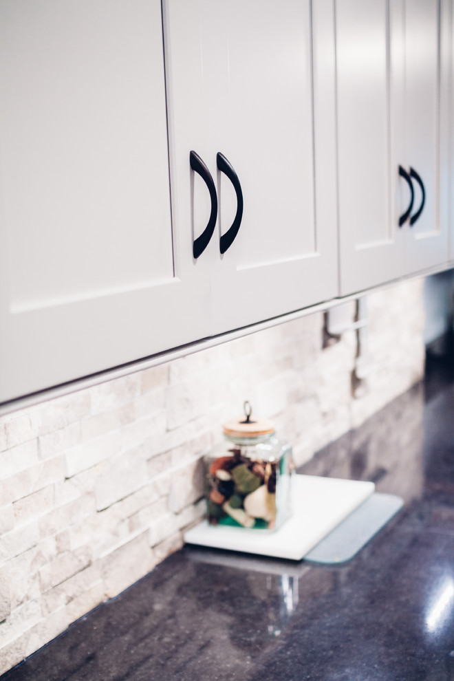 Example of a large transitional galley light wood floor and brown floor open concept kitchen design with an undermount sink, shaker cabinets, white cabinets, quartz countertops, white backsplash, stone tile backsplash, stainless steel appliances and a peninsula
