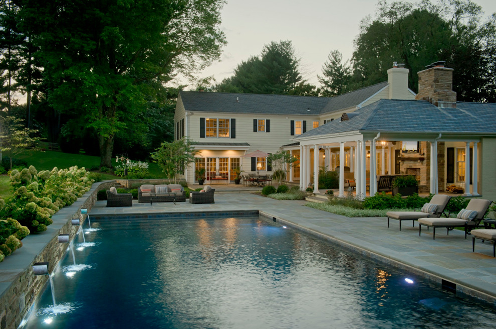 Ejemplo de piscina infinita clásica rectangular en patio trasero con adoquines de piedra natural
