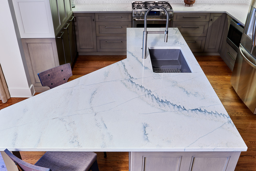 Mid-sized minimalist u-shaped medium tone wood floor and brown floor open concept kitchen photo with an undermount sink, recessed-panel cabinets, beige cabinets, granite countertops, white backsplash, ceramic backsplash, stainless steel appliances, an island and white countertops