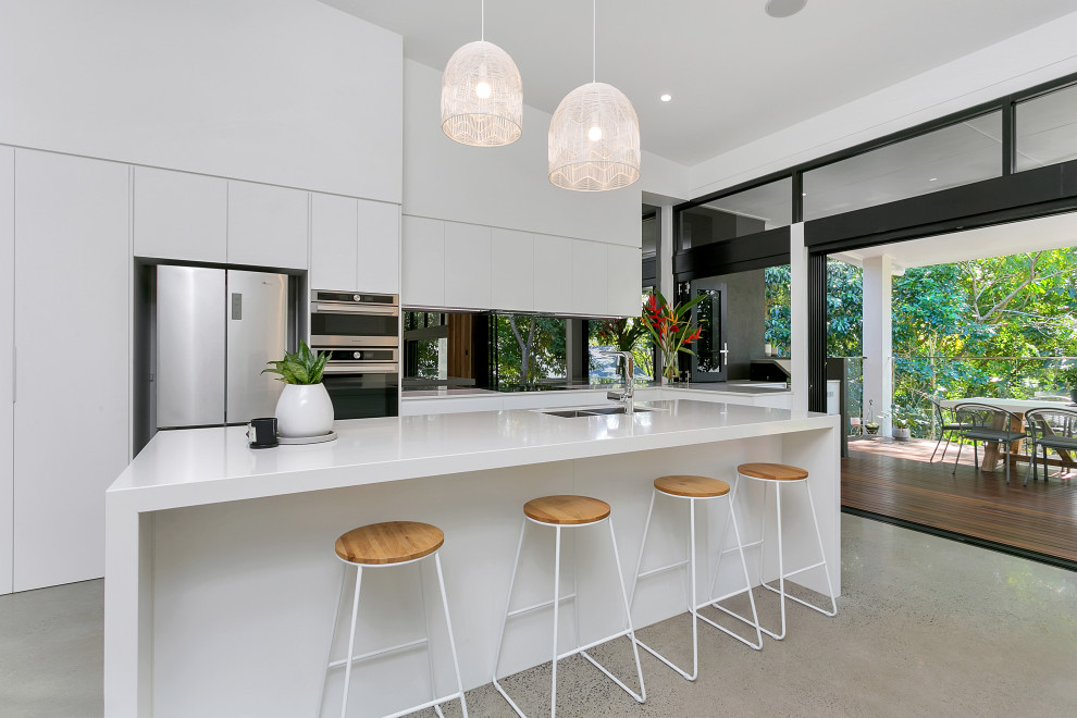 Photo of a contemporary galley kitchen in Cairns with an undermount sink, flat-panel cabinets, white cabinets, stainless steel appliances, concrete floors, with island and grey floor.