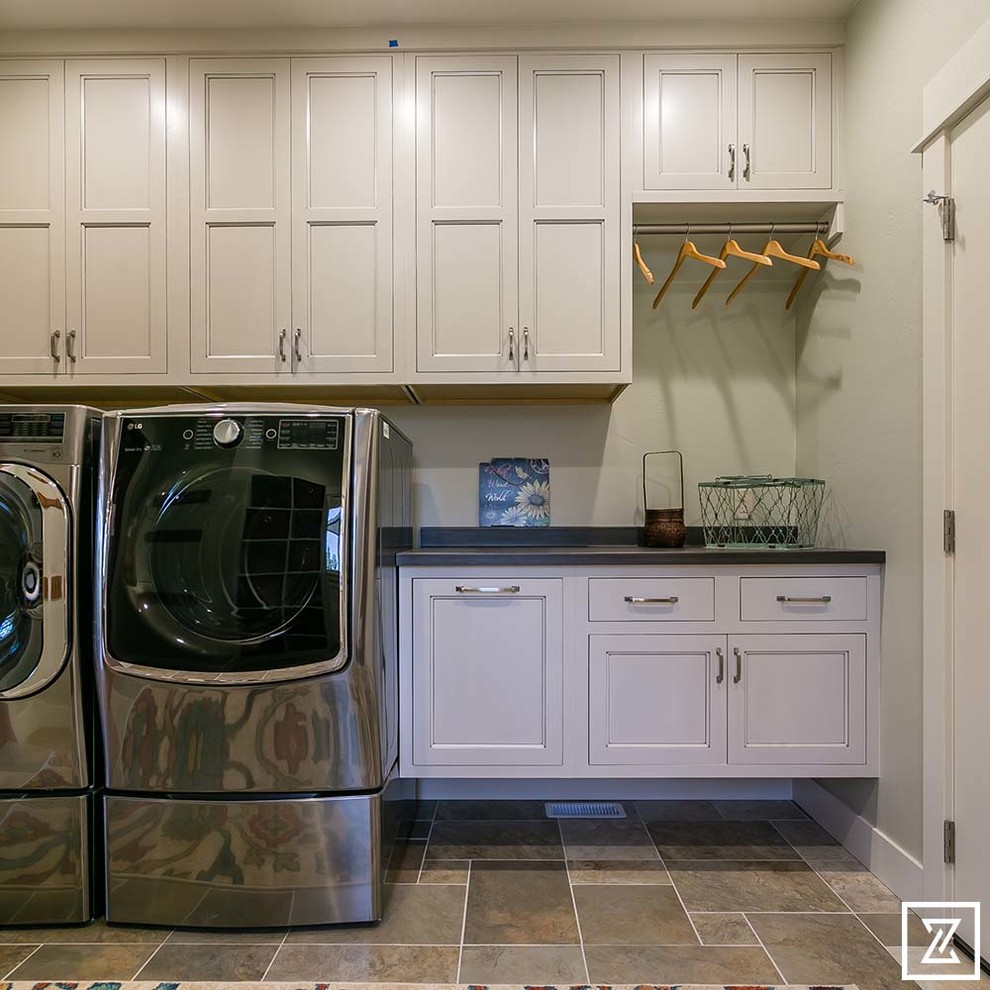 Photo of a mid-sized arts and crafts single-wall dedicated laundry room in Other with shaker cabinets, white cabinets, white walls, slate floors and a side-by-side washer and dryer.