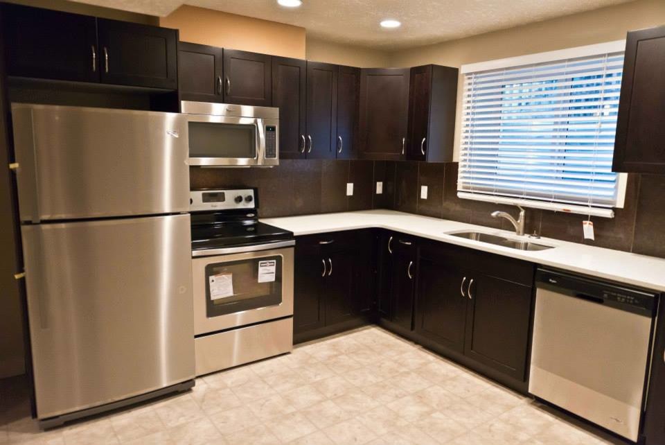 Inspiration for a small transitional l-shaped ceramic tile enclosed kitchen remodel in Edmonton with a double-bowl sink, recessed-panel cabinets, dark wood cabinets, solid surface countertops, brown backsplash, ceramic backsplash, stainless steel appliances and no island