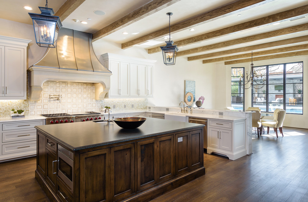This is an example of a large mediterranean l-shaped eat-in kitchen in Dallas with a farmhouse sink, white cabinets, granite benchtops, multi-coloured splashback, stainless steel appliances, with island, brown floor, shaker cabinets and dark hardwood floors.