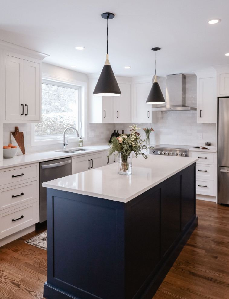 Example of a small transitional u-shaped medium tone wood floor and brown floor eat-in kitchen design in Ottawa with an undermount sink, shaker cabinets, white cabinets, quartz countertops, white backsplash, subway tile backsplash, stainless steel appliances, an island and white countertops