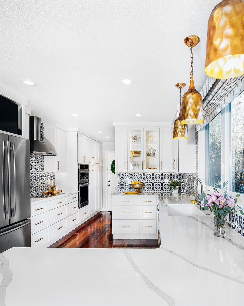 Example of a transitional l-shaped dark wood floor and brown floor kitchen design in Denver with an undermount sink, shaker cabinets, white cabinets, quartzite countertops, blue backsplash, ceramic backsplash, stainless steel appliances and white countertops