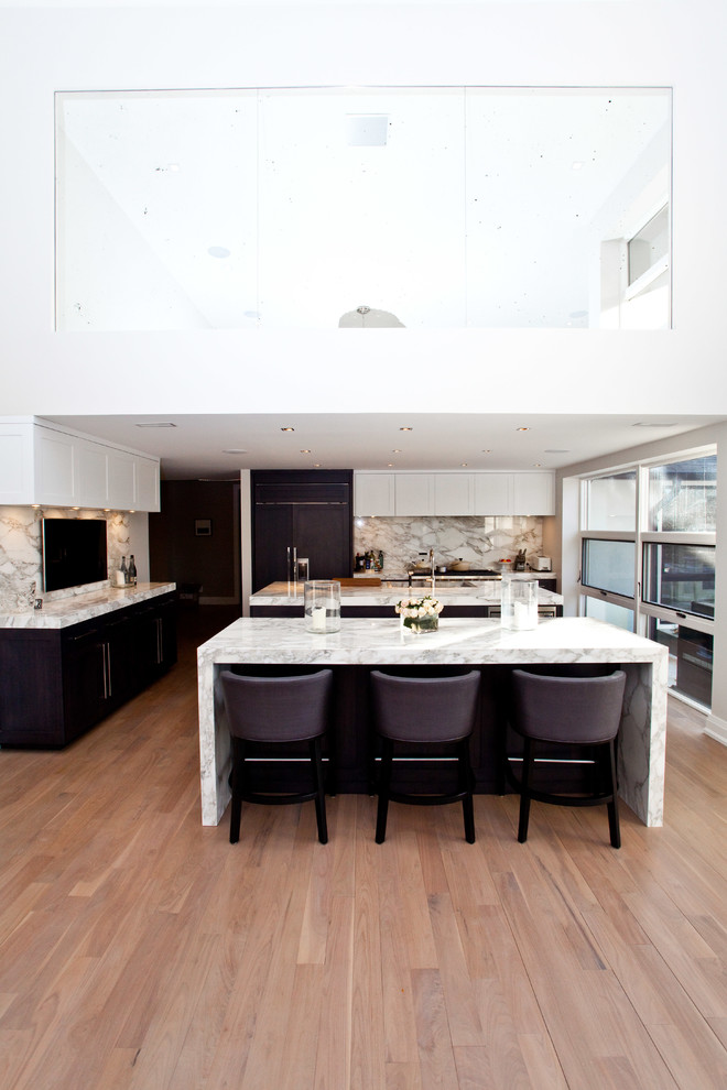 Inspiration for a large contemporary galley eat-in kitchen in Toronto with shaker cabinets, white cabinets, panelled appliances, a farmhouse sink, marble benchtops, stone slab splashback, light hardwood floors and multiple islands.