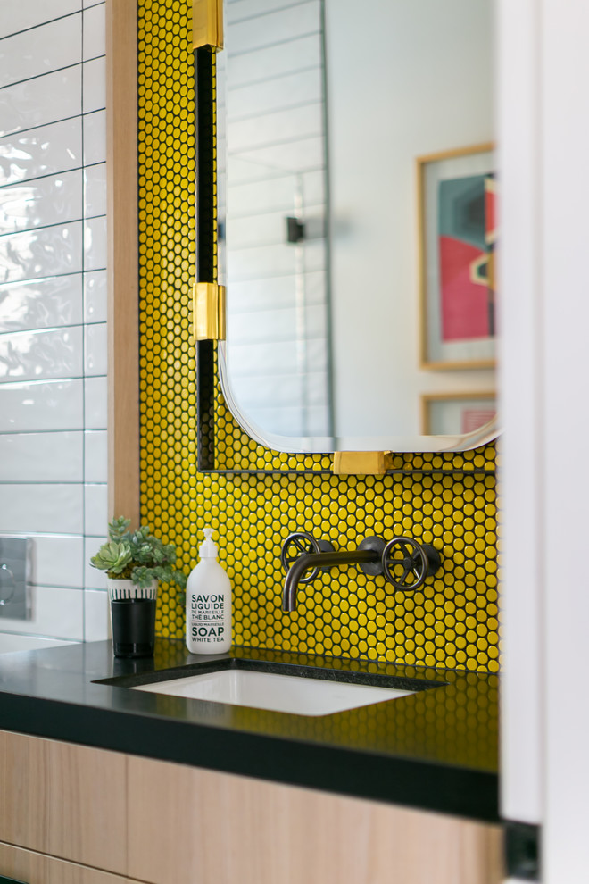 This is an example of a mid-sized modern bathroom in Orange County with flat-panel cabinets, light wood cabinets, a wall-mount toilet, yellow tile, mosaic tile, white walls, an undermount sink, black floor and black benchtops.