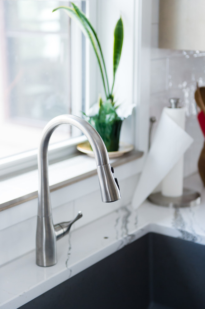 Mid-sized transitional u-shaped vinyl floor and brown floor enclosed kitchen photo with an undermount sink, flat-panel cabinets, beige cabinets, quartz countertops, white backsplash, subway tile backsplash, black appliances, a peninsula and white countertops