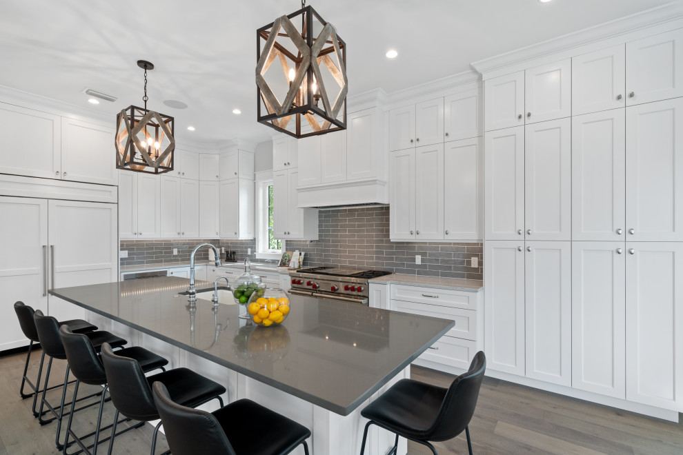 Photo of a large transitional l-shaped kitchen in Tampa with an undermount sink, shaker cabinets, white cabinets, grey splashback, subway tile splashback, panelled appliances, light hardwood floors, with island, grey floor and grey benchtop.