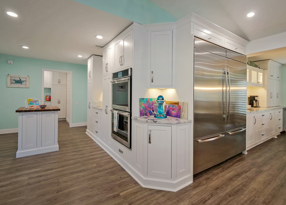 This is an example of a large tropical open plan kitchen in Jacksonville with shaker cabinets, white cabinets, quartz benchtops, white splashback, ceramic splashback, stainless steel appliances, vinyl floors, multiple islands and grey benchtop.