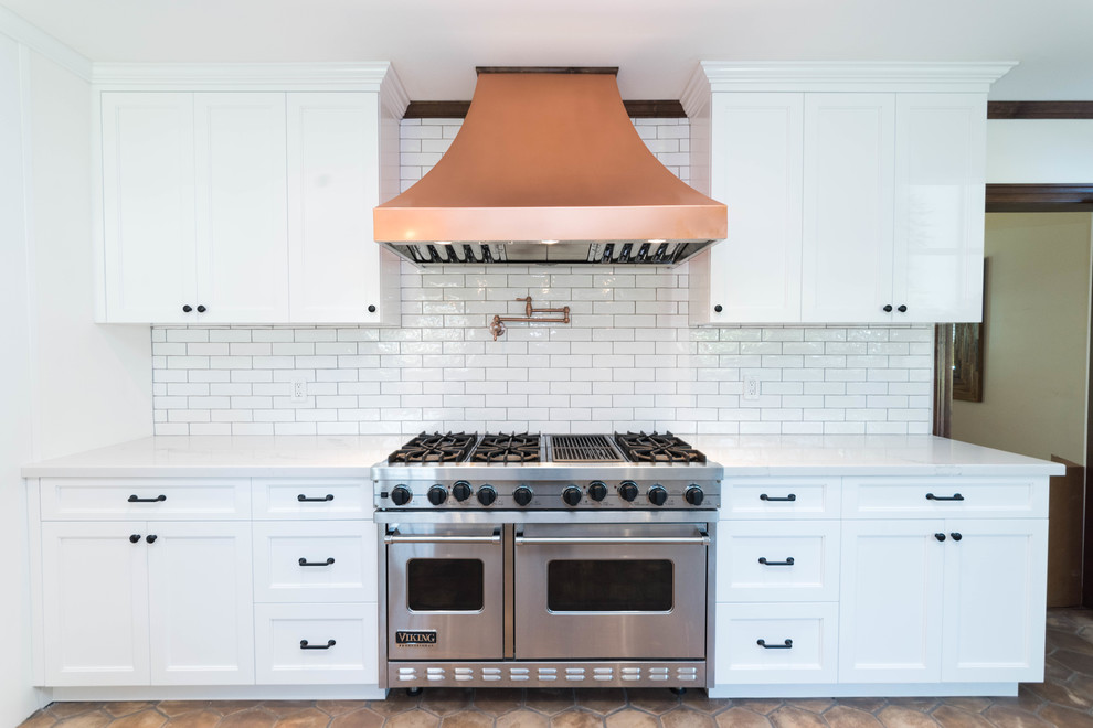 Photo of a mid-sized industrial u-shaped eat-in kitchen in San Francisco with flat-panel cabinets, white cabinets, a farmhouse sink, quartzite benchtops, ceramic splashback, stainless steel appliances, terra-cotta floors and brown floor.