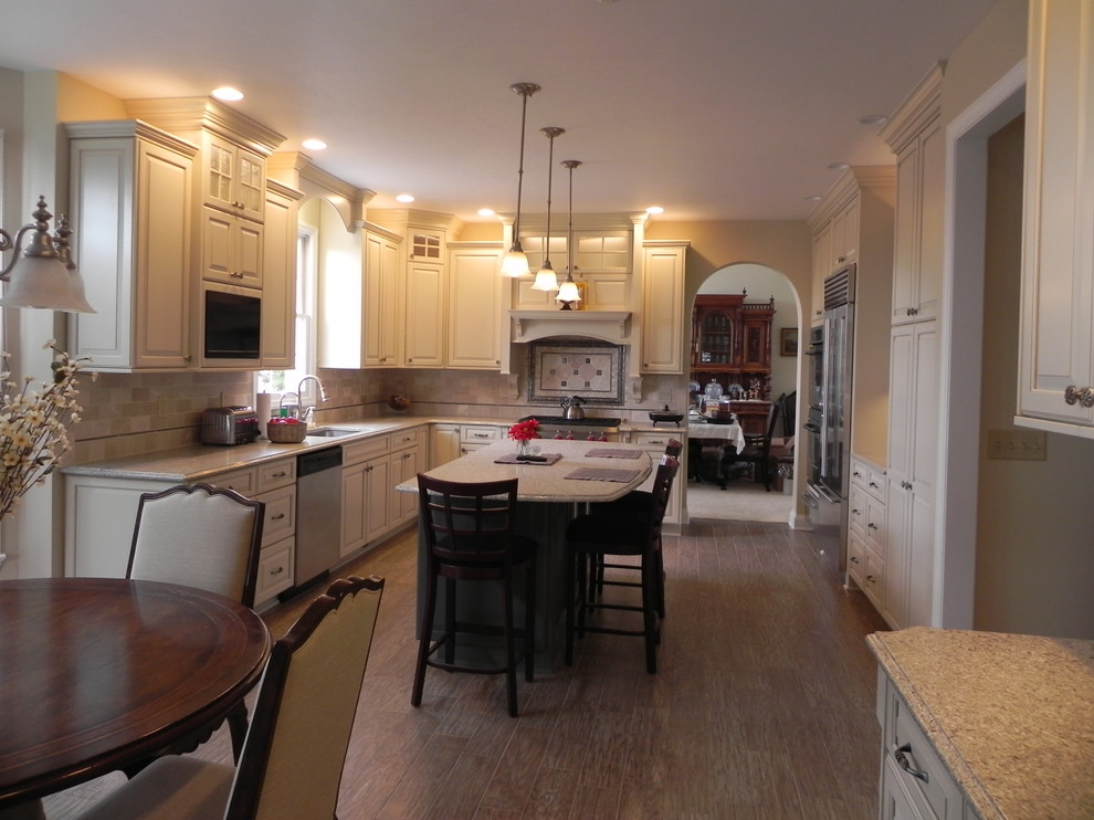 Inspiration for a mid-sized transitional u-shaped light wood floor and brown floor eat-in kitchen remodel with an undermount sink, raised-panel cabinets, white cabinets, granite countertops, beige backsplash, ceramic backsplash, stainless steel appliances and an island
