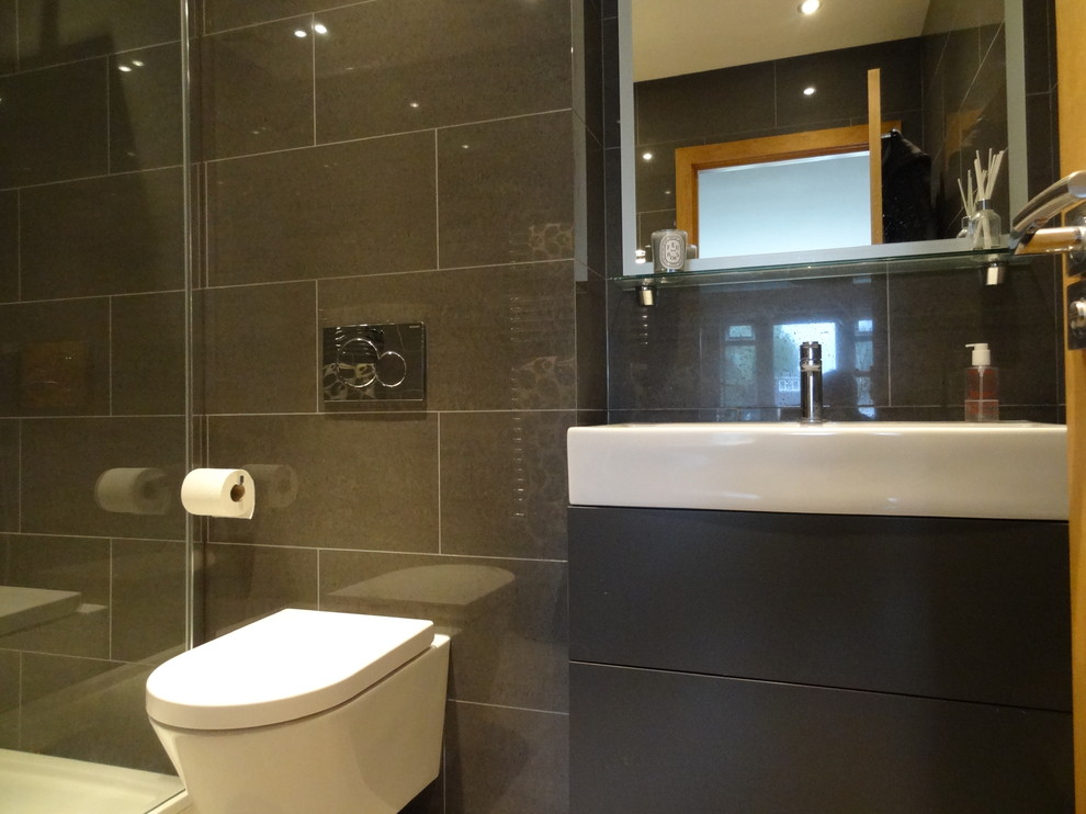 This is an example of a mid-sized modern master bathroom in London with a wall-mount sink, glass-front cabinets, light wood cabinets, quartzite benchtops, a double shower, a one-piece toilet, brown tile, ceramic tile, grey walls and ceramic floors.