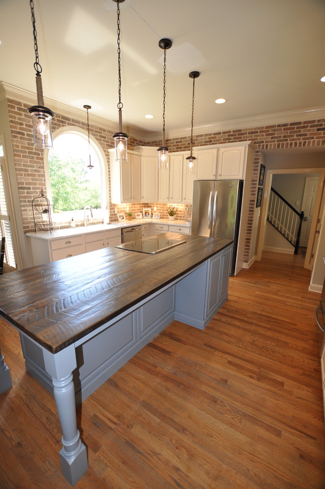 Mid-sized country l-shaped eat-in kitchen in Atlanta with an undermount sink, raised-panel cabinets, white cabinets, wood benchtops, brown splashback, brick splashback, stainless steel appliances, dark hardwood floors, with island and brown floor.