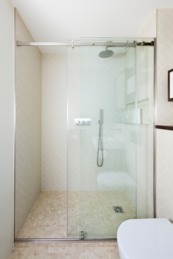 This is an example of a mid-sized midcentury 3/4 bathroom in London with glass-front cabinets, brown cabinets, an open shower, a wall-mount toilet, beige tile, porcelain tile, beige walls, a wall-mount sink, beige floor and a sliding shower screen.