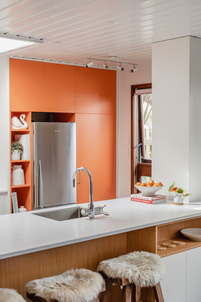Immagine di una cucina moderna di medie dimensioni con lavello a vasca singola, ante lisce, ante arancioni, top in superficie solida, elettrodomestici in acciaio inossidabile, pavimento in cemento, penisola, pavimento grigio, top bianco e soffitto in legno