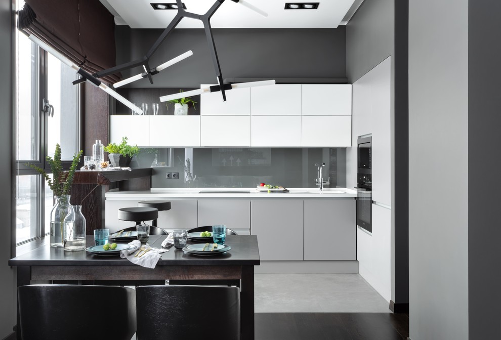 This is an example of a mid-sized contemporary l-shaped open plan kitchen in Moscow with an integrated sink, flat-panel cabinets, white cabinets, solid surface benchtops, grey splashback, black appliances, porcelain floors, no island, grey floor, white benchtop and glass sheet splashback.