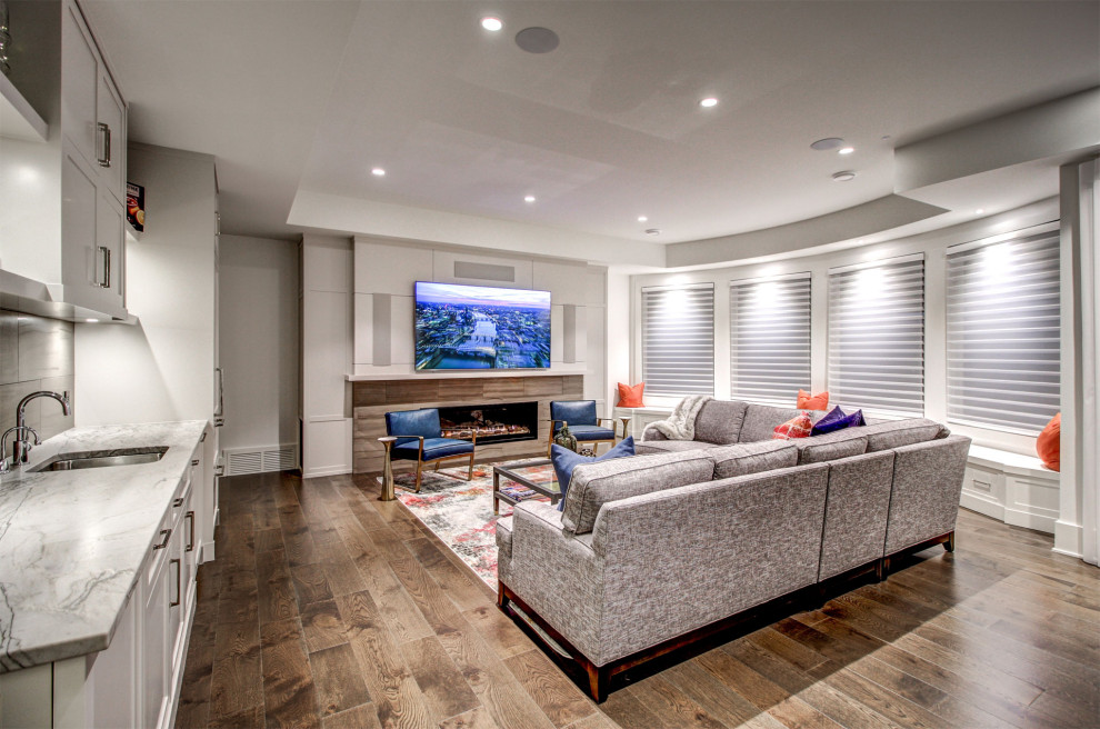 Design ideas for a large contemporary open concept family room in Calgary with a home bar, white walls, medium hardwood floors, a standard fireplace, a stone fireplace surround, a wall-mounted tv and brown floor.
