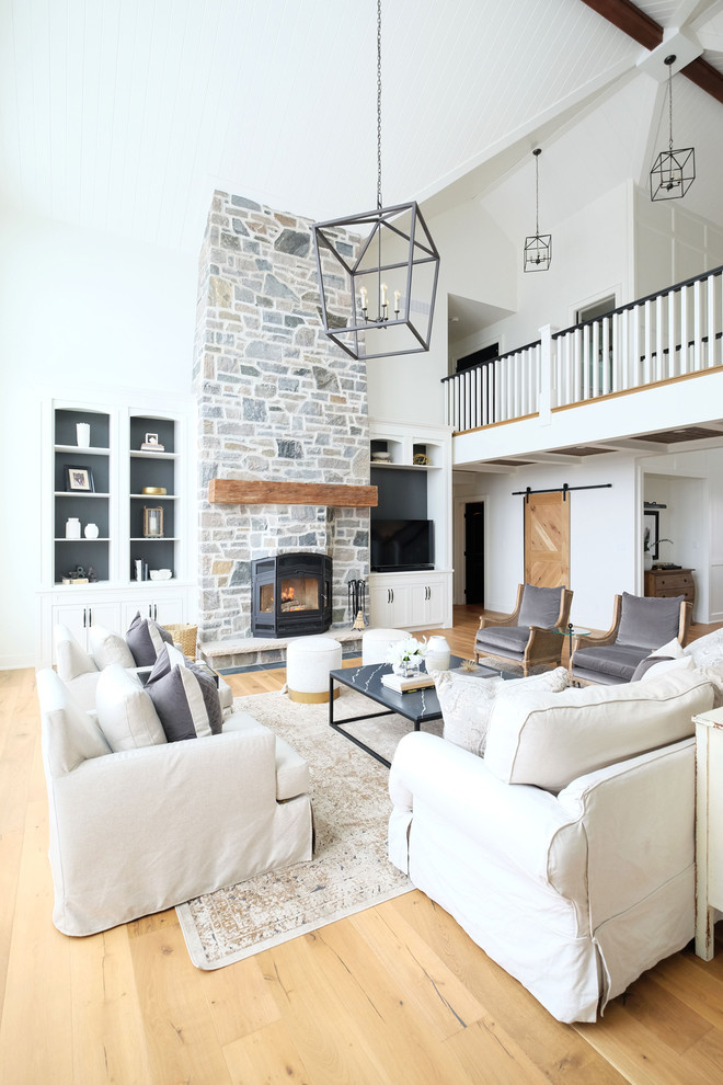 Country open concept family room in Toronto with white walls, light hardwood floors, a stone fireplace surround and a freestanding tv.