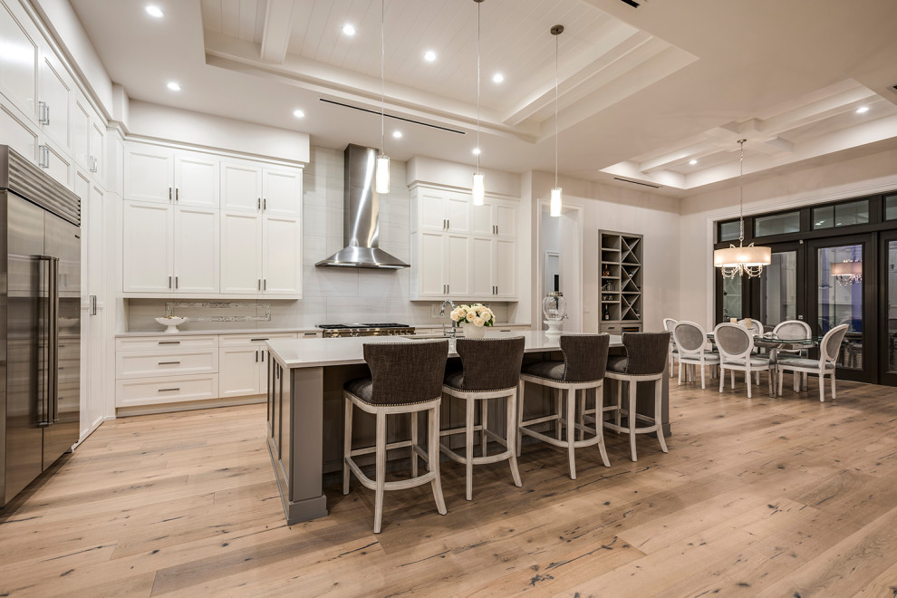 This is an example of a mid-sized beach style l-shaped open plan kitchen in Other with recessed-panel cabinets, white cabinets, stainless steel appliances, medium hardwood floors, with island and coffered.