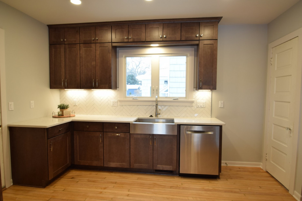 Example of a transitional light wood floor eat-in kitchen design with a farmhouse sink, shaker cabinets, medium tone wood cabinets, quartz countertops, white backsplash, ceramic backsplash, stainless steel appliances and a peninsula