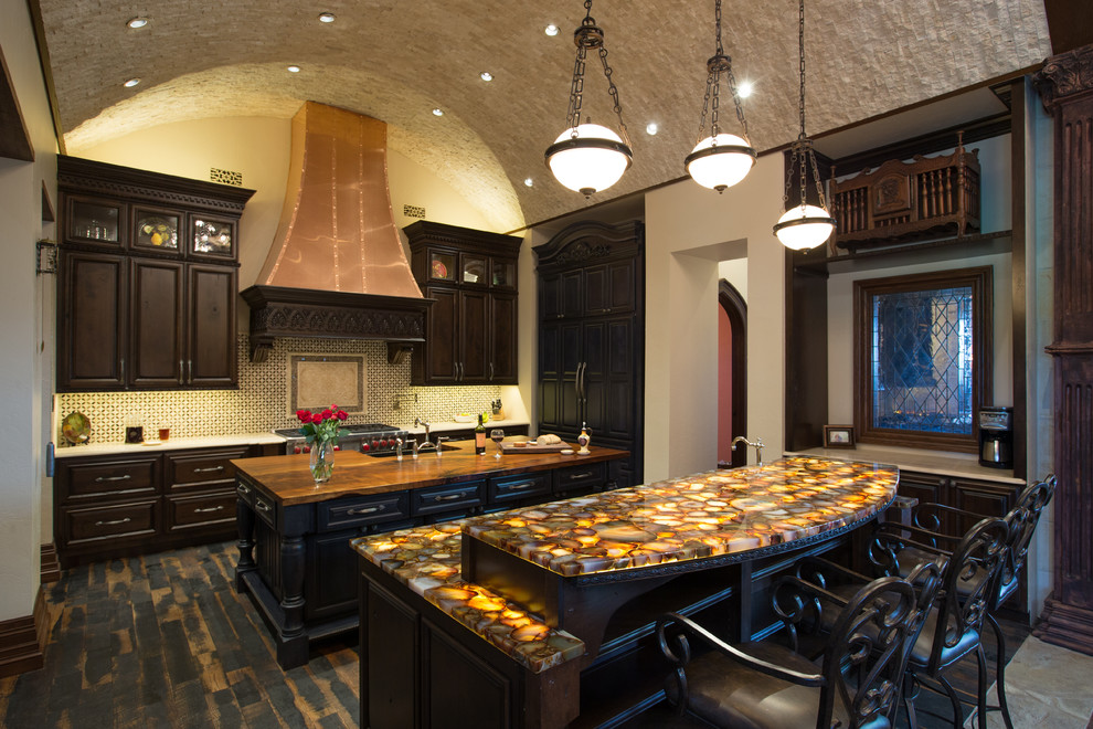 Large traditional l-shaped eat-in kitchen in Austin with a farmhouse sink, raised-panel cabinets, dark wood cabinets, onyx benchtops, multi-coloured splashback, cement tile splashback, panelled appliances, dark hardwood floors, multiple islands, brown floor and brown benchtop.