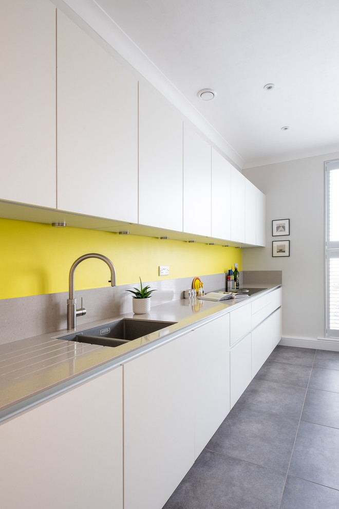 Photo of a small modern galley eat-in kitchen in Gloucestershire with flat-panel cabinets, white cabinets, quartzite benchtops, yellow splashback, black appliances, porcelain floors, grey floor and grey benchtop.