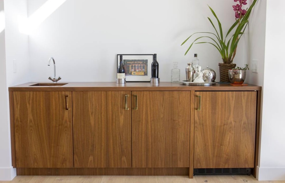 Photo of a mid-sized modern single-wall bar cart in Phoenix with an undermount sink, flat-panel cabinets, medium wood cabinets, wood benchtops, white splashback, light hardwood floors, beige floor and brown benchtop.
