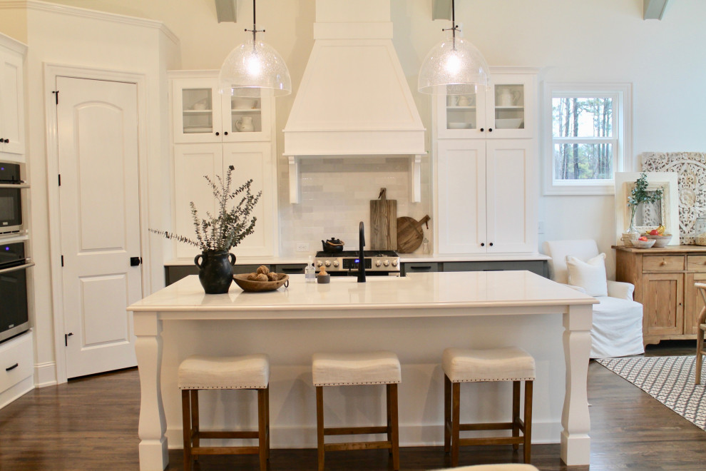 Photo of a large l-shaped eat-in kitchen in Raleigh with a farmhouse sink, shaker cabinets, white cabinets, quartzite benchtops, white splashback, subway tile splashback, stainless steel appliances, dark hardwood floors, with island, white benchtop and vaulted.