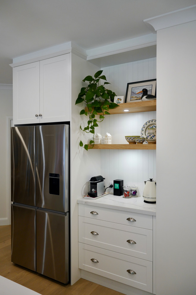 Photo of a large traditional l-shaped eat-in kitchen in Sydney with a farmhouse sink, shaker cabinets, white cabinets, quartz benchtops, white splashback, subway tile splashback, black appliances, medium hardwood floors, with island, brown floor and white benchtop.
