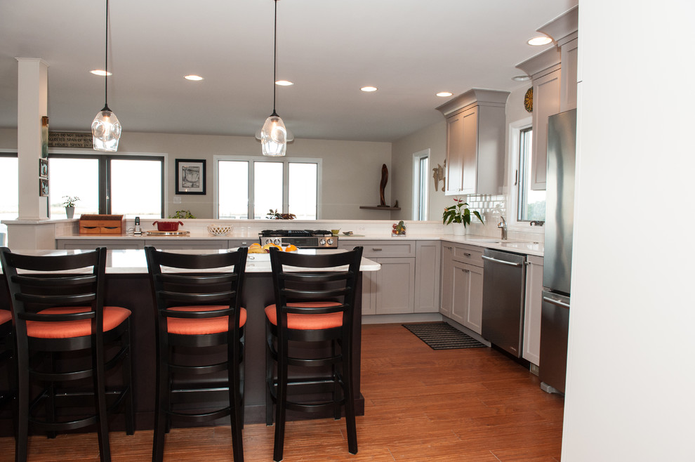 Inspiration for a large transitional l-shaped dark wood floor and brown floor eat-in kitchen remodel in Philadelphia with an undermount sink, shaker cabinets, white cabinets, quartz countertops, white backsplash, subway tile backsplash, stainless steel appliances and a peninsula