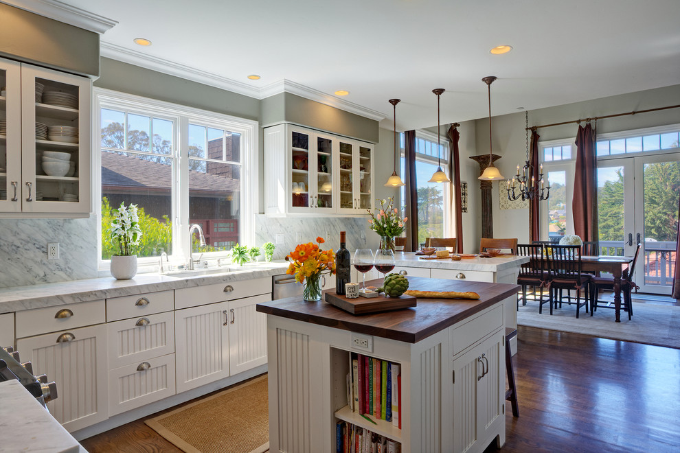 Open concept kitchen - large traditional u-shaped dark wood floor open concept kitchen idea in San Francisco with an undermount sink, shaker cabinets, white cabinets, marble countertops, white backsplash, stone slab backsplash, stainless steel appliances and an island