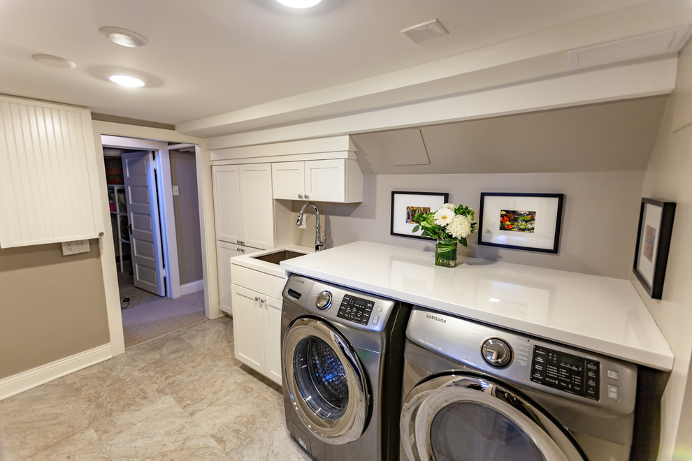 Photo of a large traditional single-wall dedicated laundry room in Minneapolis with an undermount sink, beaded inset cabinets, white cabinets, marble benchtops, beige walls, vinyl floors, a side-by-side washer and dryer, beige floor and white benchtop.