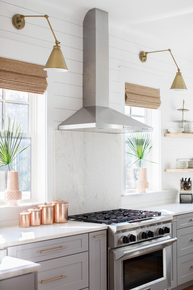 Inspiration for a beach style u-shaped kitchen in Charleston with a farmhouse sink, shaker cabinets, grey cabinets, white splashback, stainless steel appliances, medium hardwood floors, with island, brown floor and white benchtop.