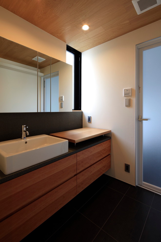 This is an example of a modern powder room in Tokyo with medium wood cabinets, white walls and a vessel sink.
