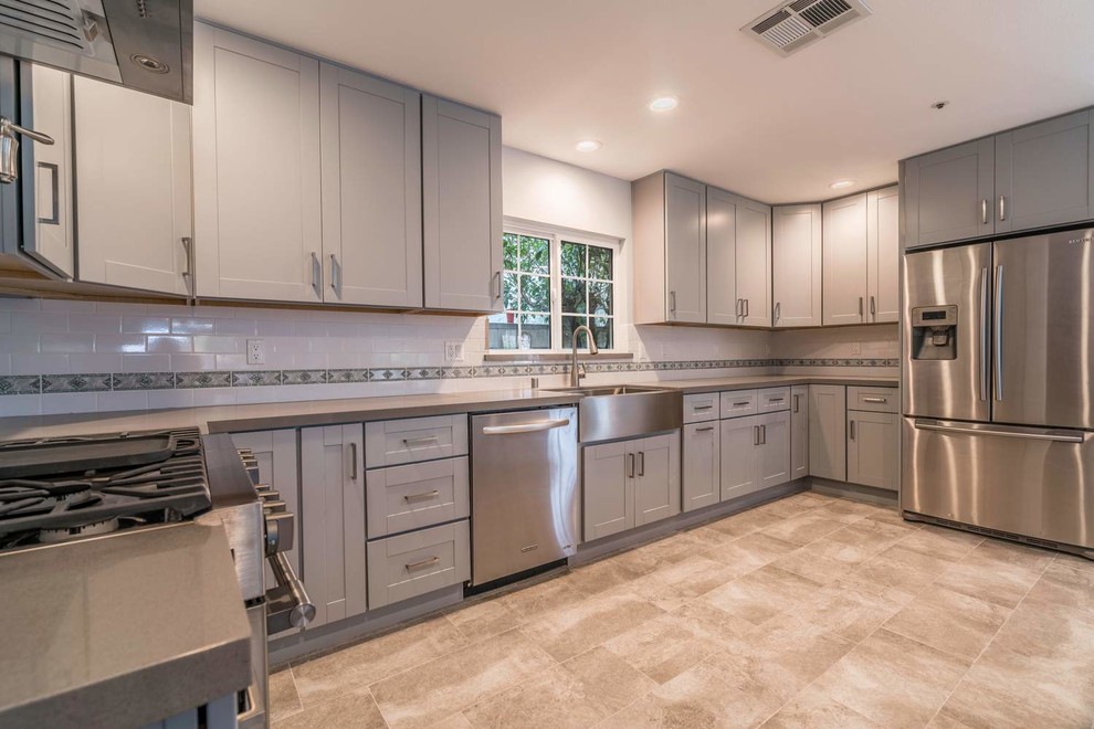 Inspiration for a mid-sized contemporary u-shaped eat-in kitchen in Orange County with a farmhouse sink, recessed-panel cabinets, grey cabinets, quartz benchtops, white splashback, subway tile splashback, stainless steel appliances, porcelain floors, with island, grey floor and white benchtop.