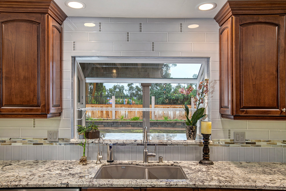 Mid-sized transitional u-shaped eat-in kitchen in San Diego with an undermount sink, raised-panel cabinets, brown cabinets, granite benchtops, grey splashback, ceramic splashback, stainless steel appliances, porcelain floors and a peninsula.