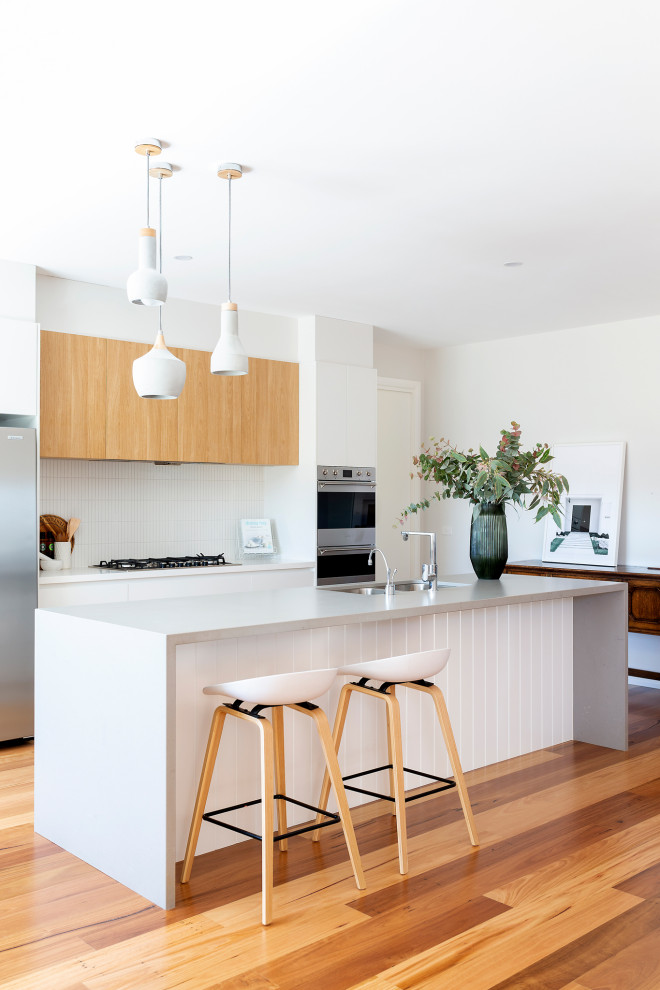 Photo of a mid-sized galley kitchen in Canberra - Queanbeyan with a double-bowl sink, quartz benchtops, white splashback, matchstick tile splashback, stainless steel appliances, medium hardwood floors, multiple islands and grey benchtop.