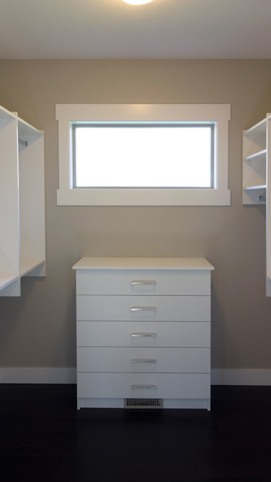 This is an example of a mid-sized transitional gender-neutral walk-in wardrobe in Vancouver with flat-panel cabinets, white cabinets and dark hardwood floors.